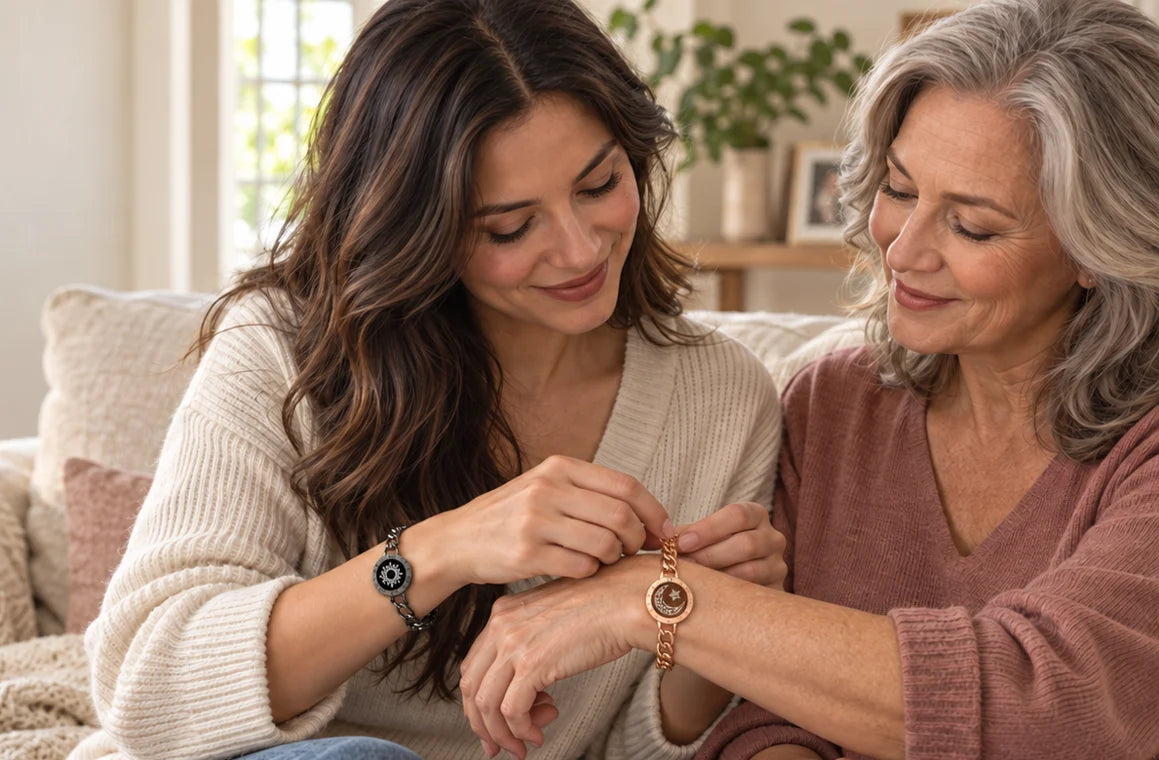 An adult daughter, already wearing a black Sun Figaro bracelet, helps fasten a rose gold Moon Figaro bracelet on her mother’s wrist