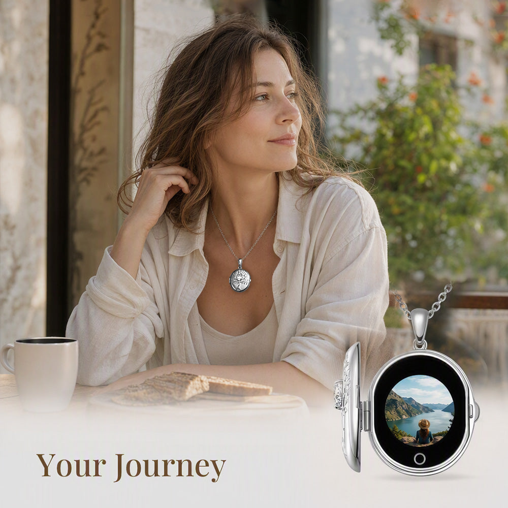 A woman seated at a table wearing a round silver pendant necklace, with a close-up inset of the necklace displayed as an open locket showing a scenic landscape photo. The text 'Your Journey' appears at the bottom.